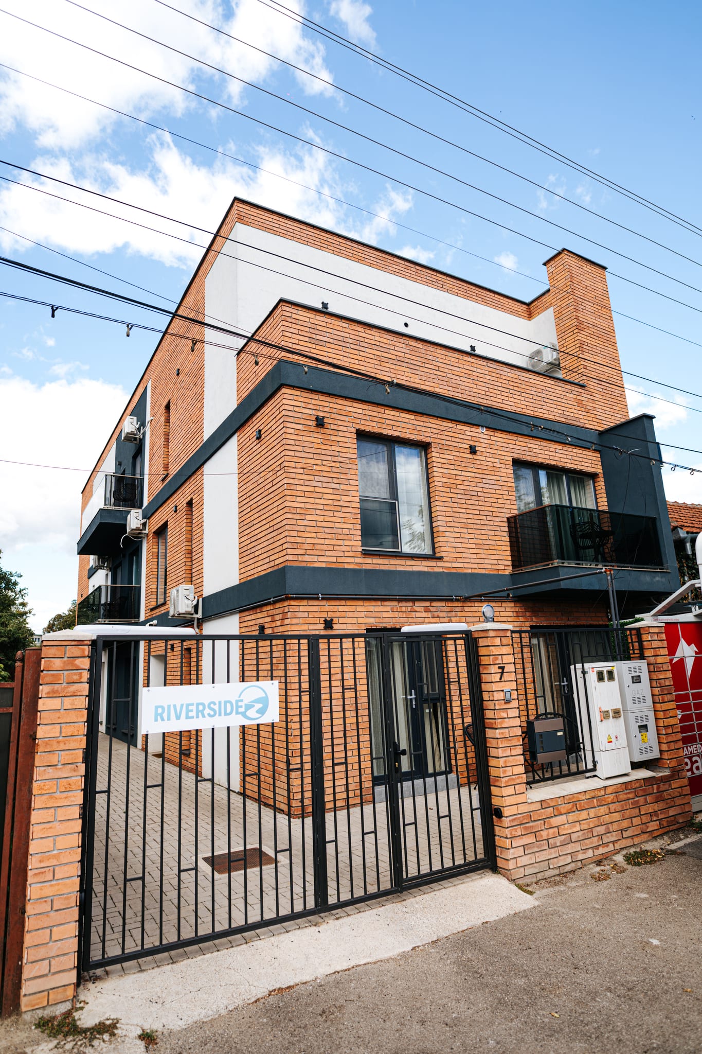 Terracotta brick and charcoal facade of Riverside ApartHotel against a blue sky